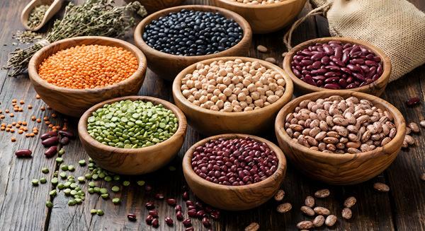 assorted legumes and grains in wooden bowls on rustic table. hea