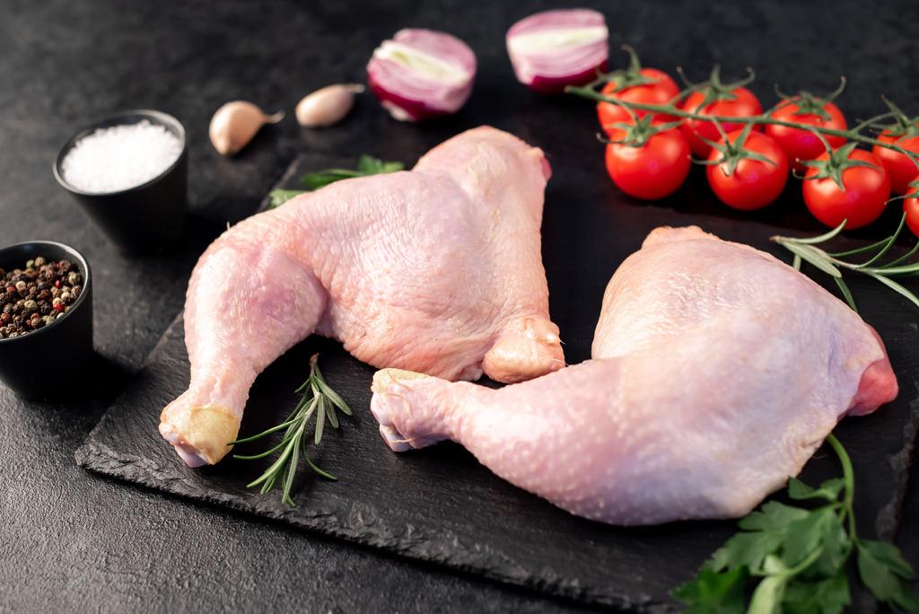 two raw chicken legs with spices and herbs on a stone background