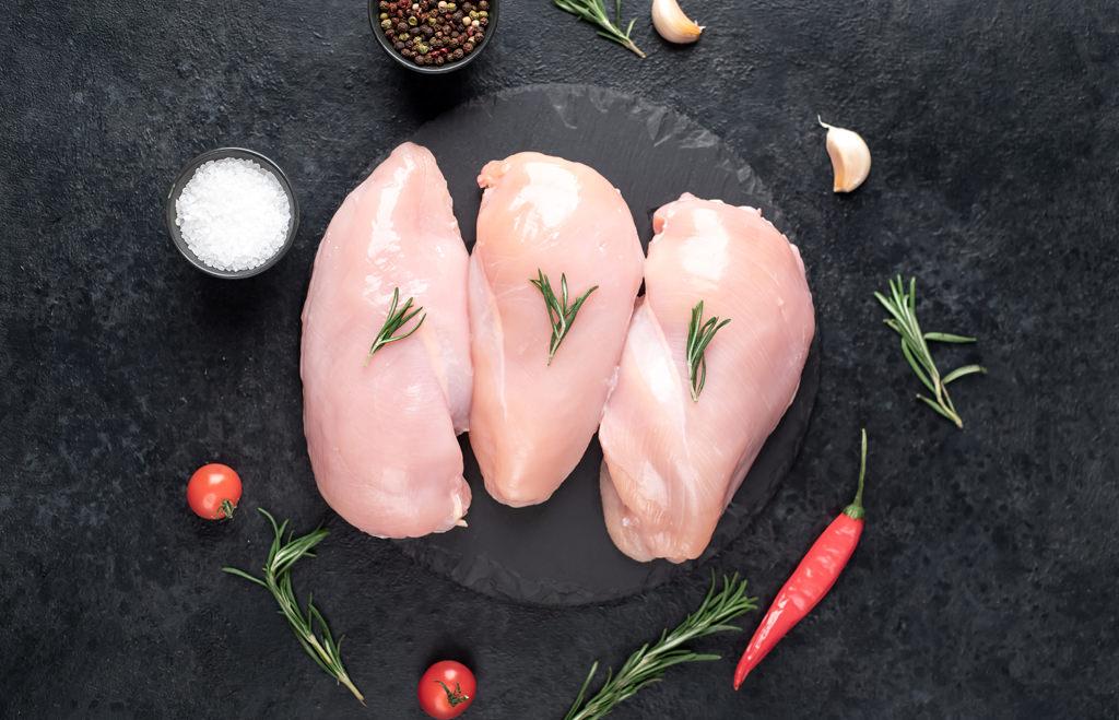 three raw chicken breasts on stone background